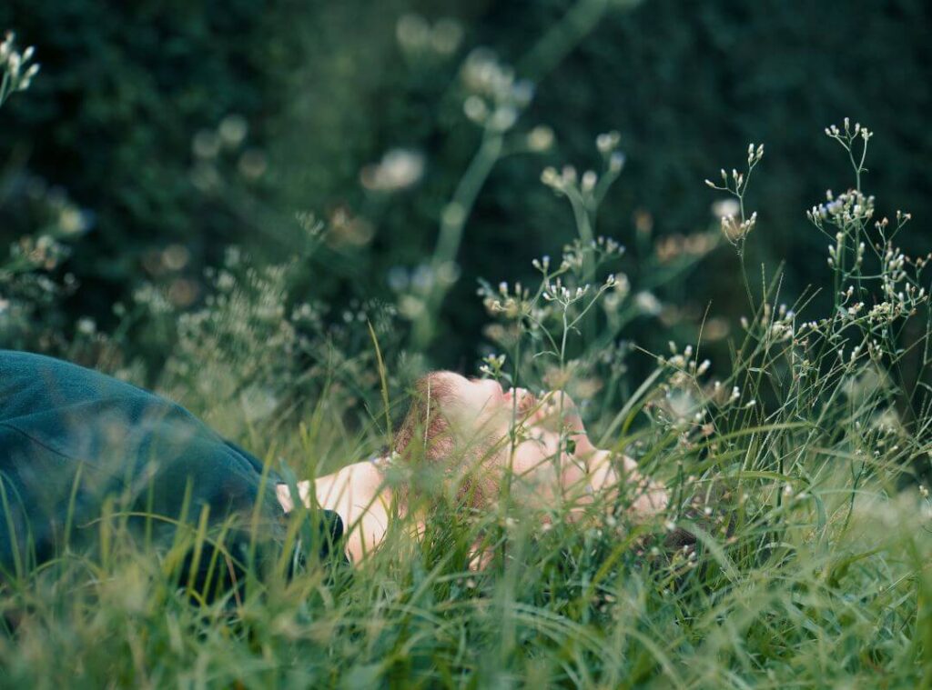 A man lies in the grass with his eyes closed